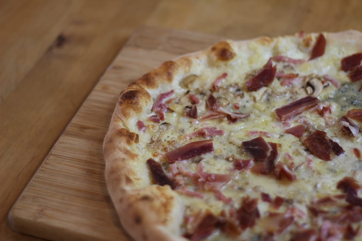 Pizza Auvergnate garnie de Crème fraîche, Champignons, Jambon de pays, Lardons, Emmental français et Roquefort