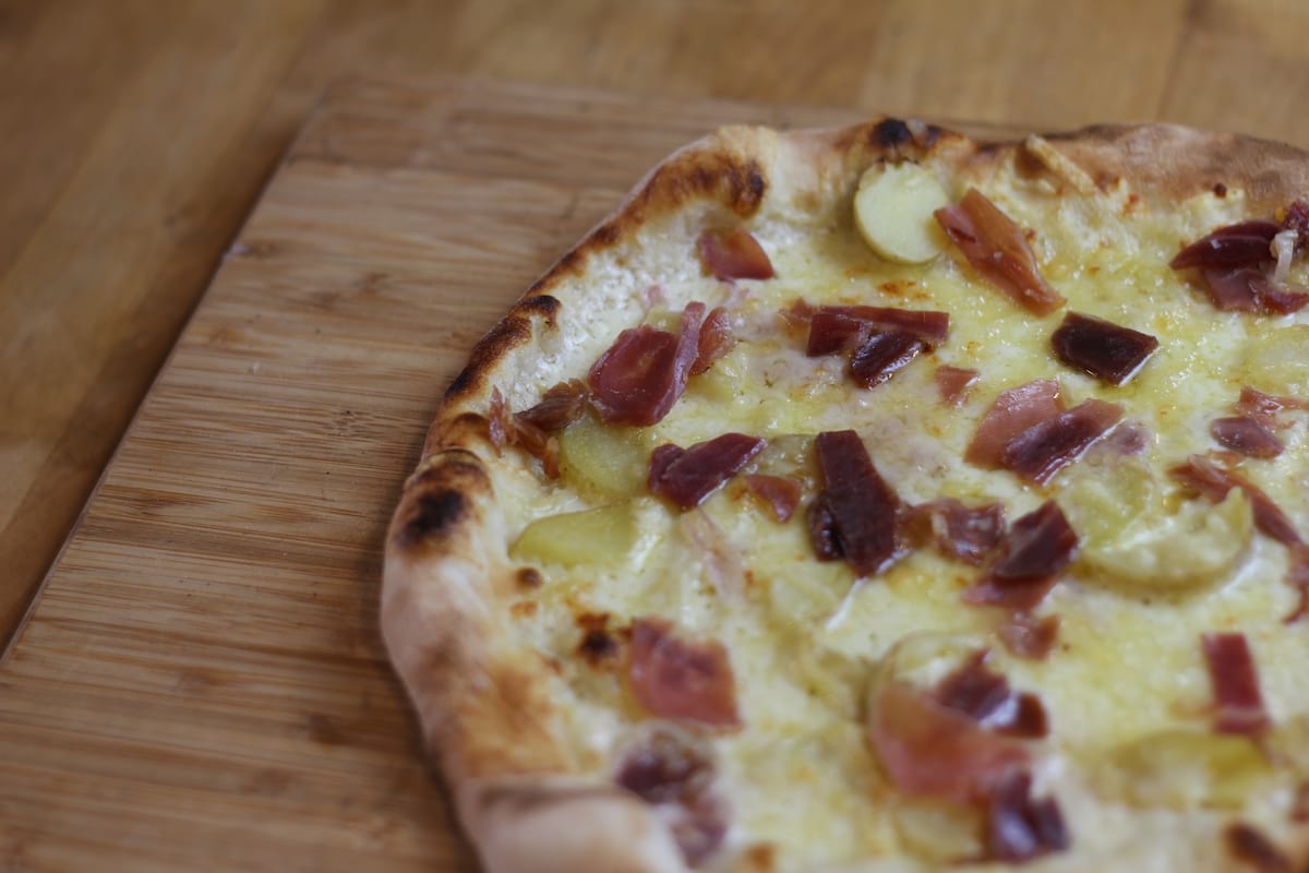 Pizza Aveyronnaise garnie de Crème fraîche, Oignons confits, Pomme de terre, Jambon de pays, Emmental français et Tome