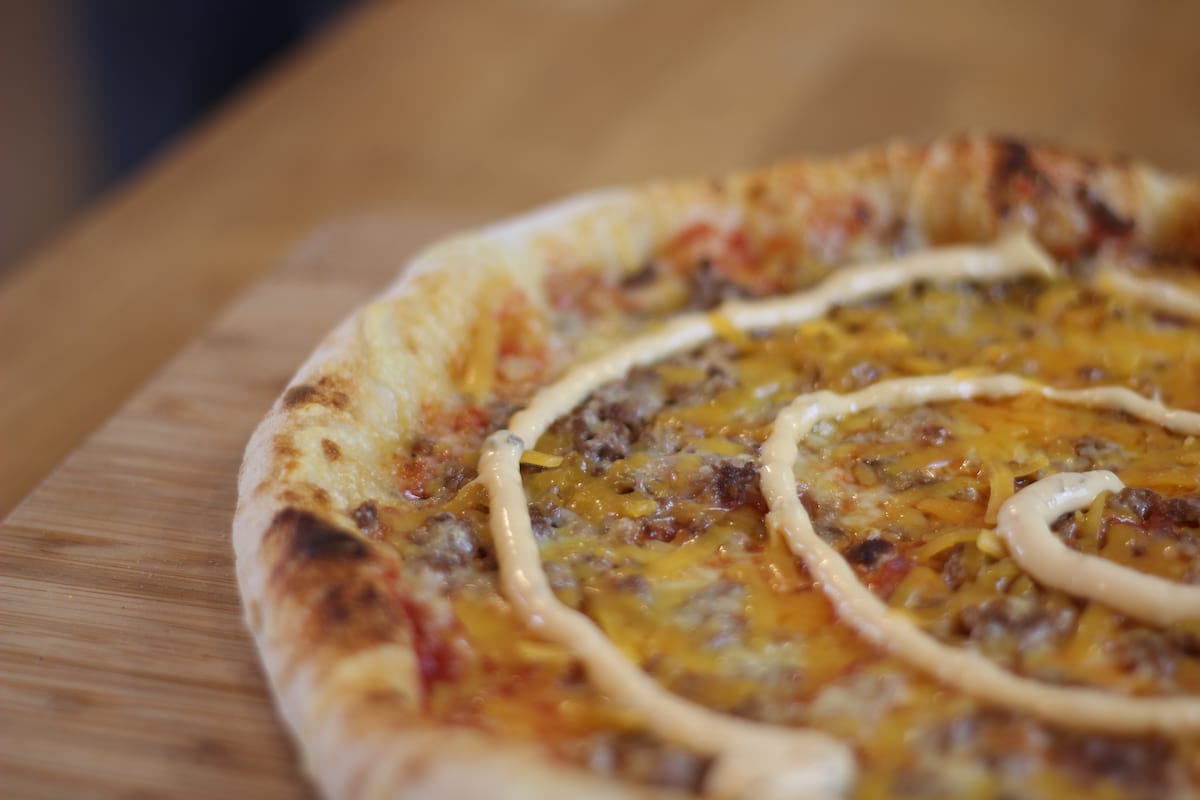 Pizza Burger garnie de Sauce tomate, Oignons confits, Steak haché, Cheddar, Emmental français et Sauce burger