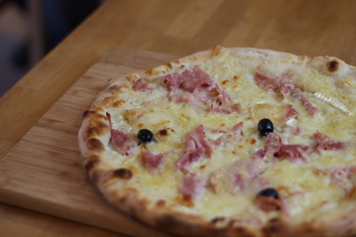 Pizza Chevrotte garnie de Crème fraîche, Jambon, Emmental français, Fromage de chèvre et Olives noires