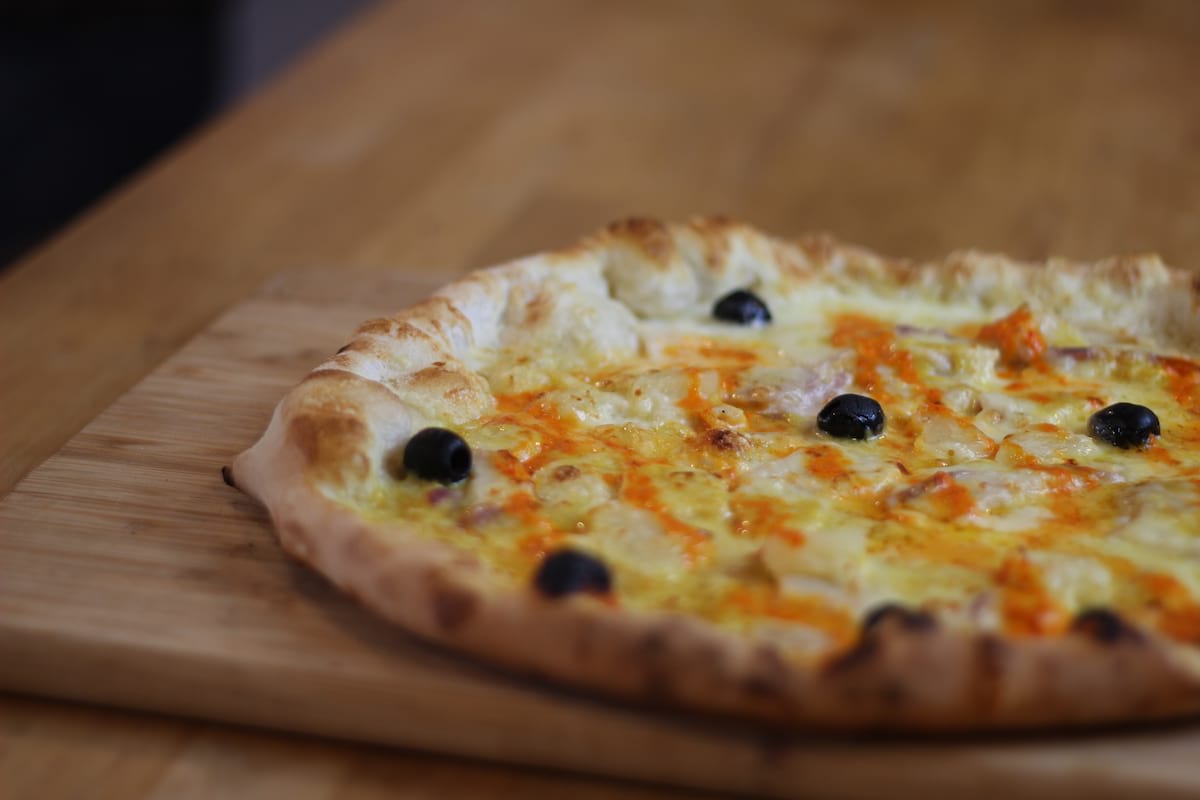 Pizza Indienne garnie de Crème fraîche, Oignons confits, Poivrons, Poulet, Emmental français, Ananas et Crème de curry