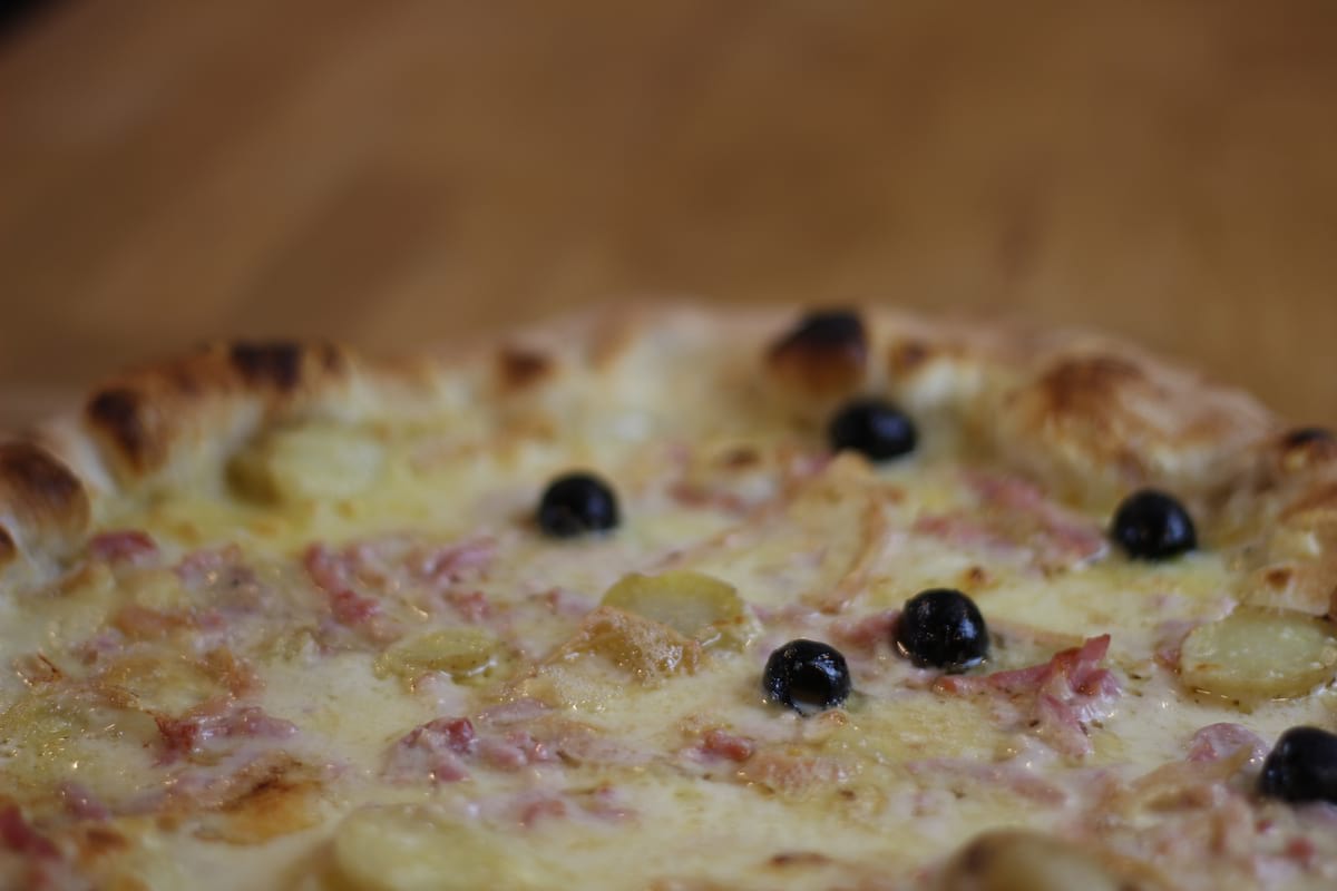 Pizza Savoyarde garnie de Crème fraîche, Oignons confits, Pomme de terre, Lardons fumés, Emmental français et Reblochon