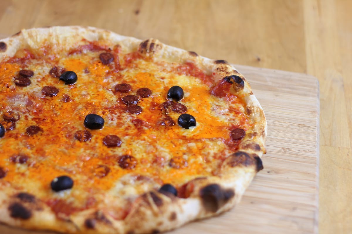 Pizza Tex-Mex garnie de Sauce tomate, Oignons frits, Poivrons, Chorizo, Merguez, Emmental français et Olives noires